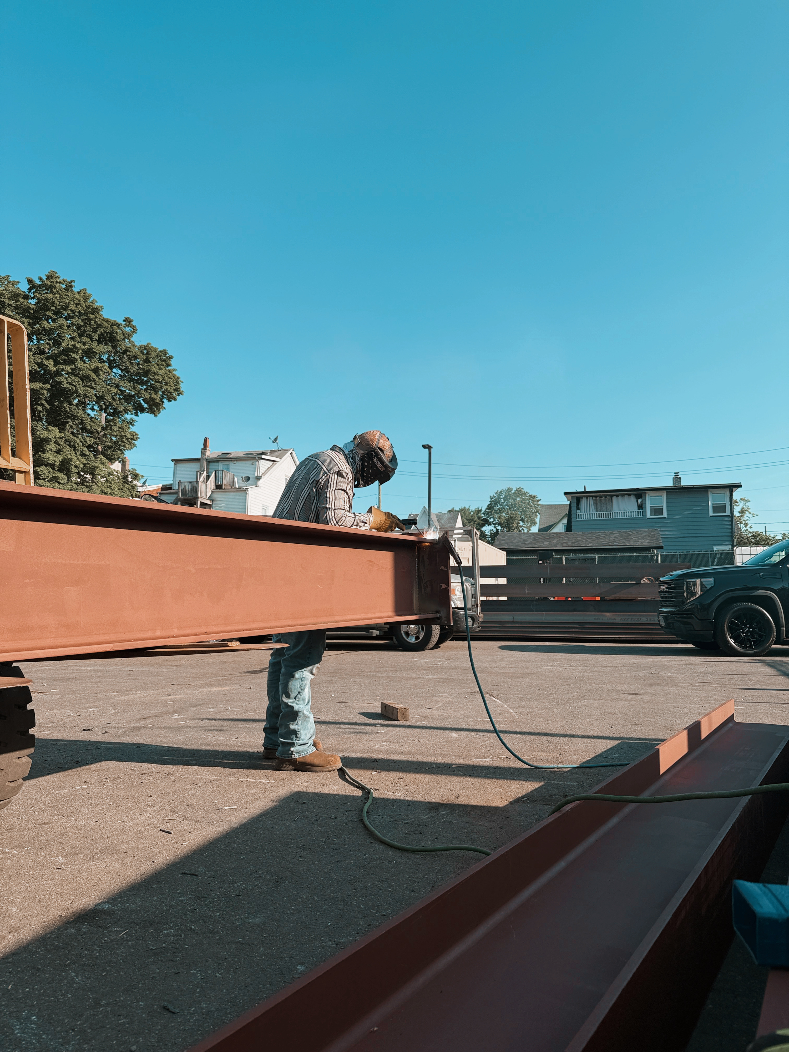 Welder on large steel trailer frame, clear sky