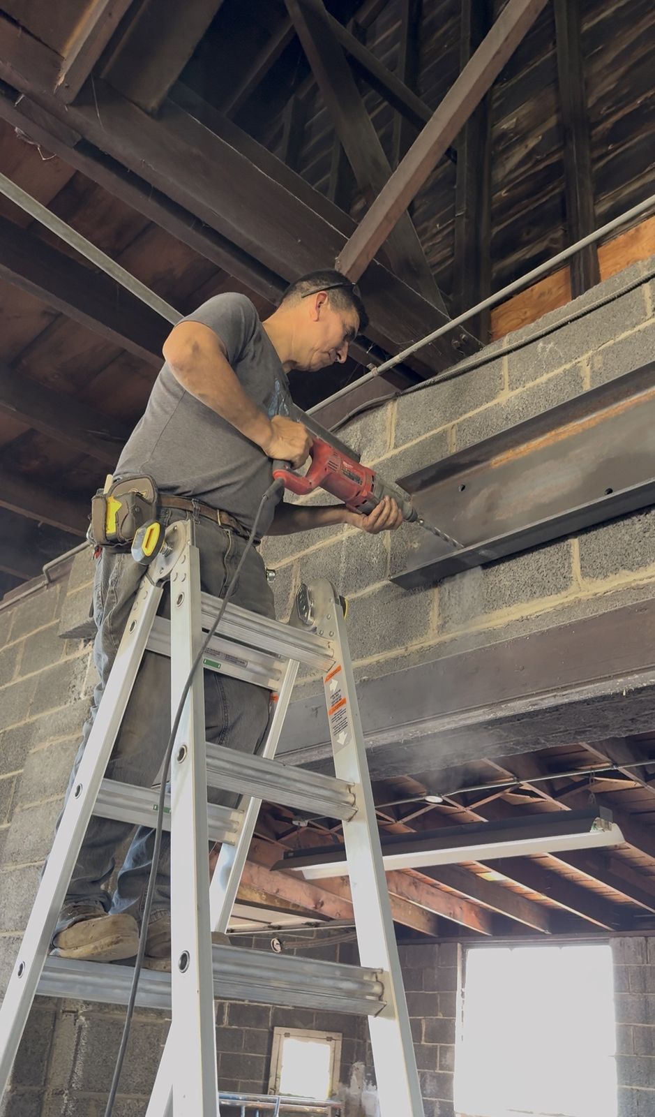 E&S crew member drilling a steel beam set on a block wall during an install